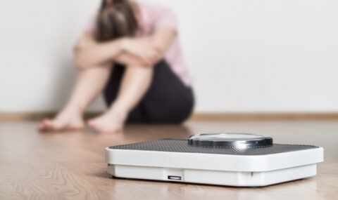 Weight loss fail concept. Scale and depressed, frustrated and sad woman sitting on floor holding head and arms on knees.