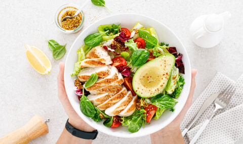 Grilled chicken meat and fresh vegetable salad of tomato, avocado, lettuce and spinach. Healthy and detox food concept. Ketogenic diet. Buddha bowl in hands on white background, top view