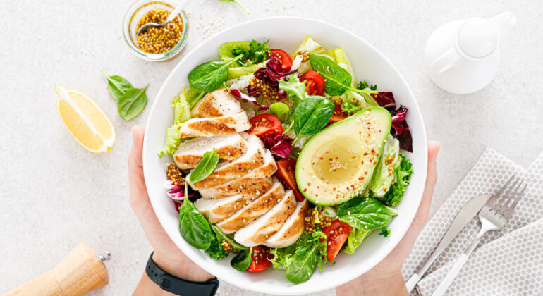 Grilled chicken meat and fresh vegetable salad of tomato, avocado, lettuce and spinach. Healthy and detox food concept. Ketogenic diet. Buddha bowl in hands on white background, top view